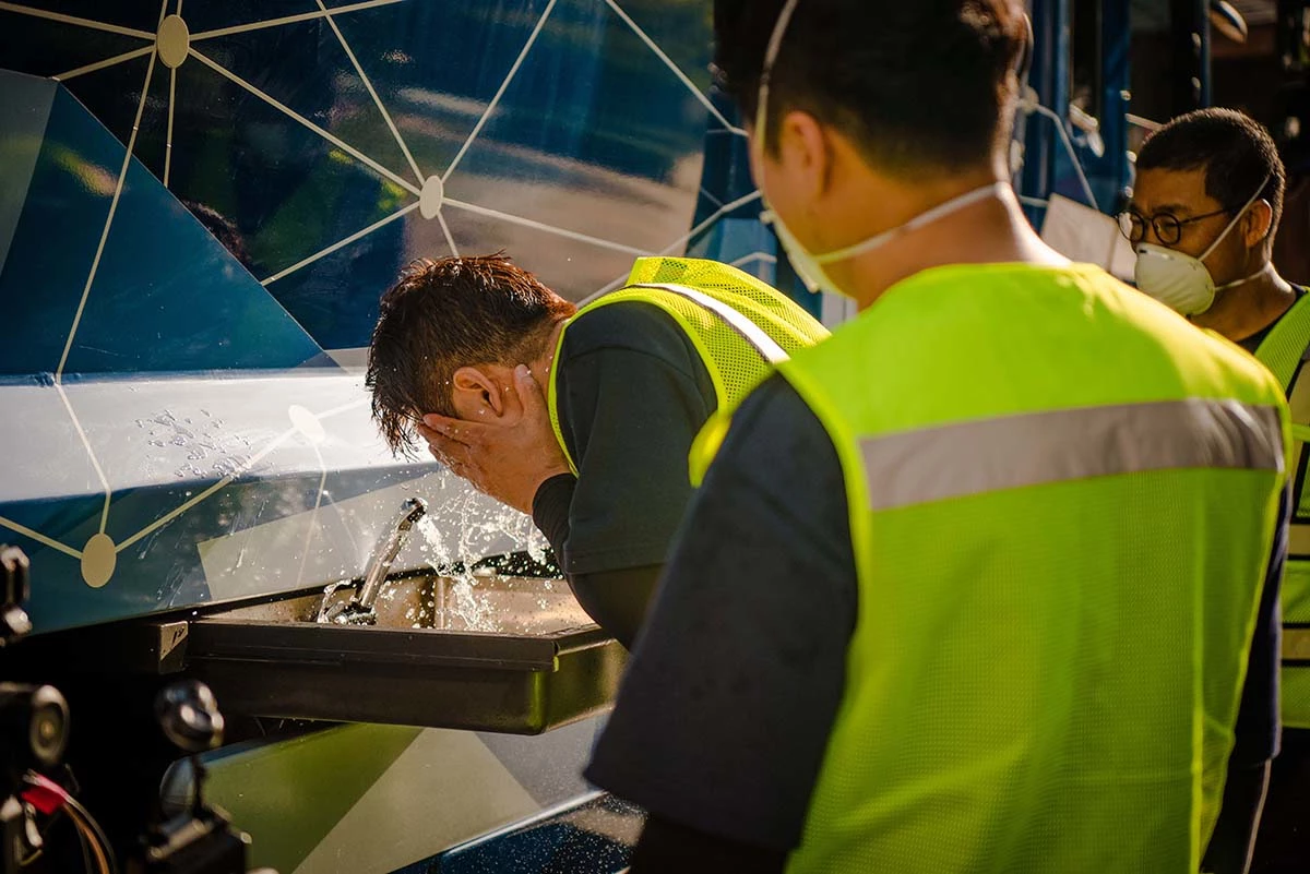 환경미화원들이 수소청소트럭에서 나오는 물로 얼굴을 씻고 있다.