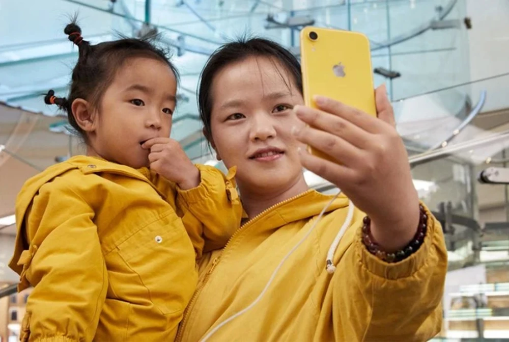 노란색 옷을 입은 모녀가 노란 색상의 아이폰을 바라보고 있다.