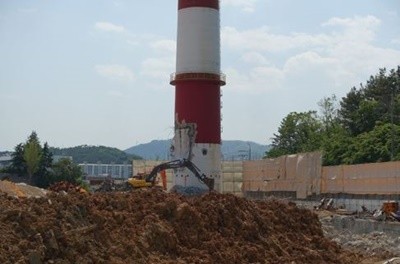 2019년 5월 17일 주민들의 항의와 기장군의 '긴급공사중지 명령'을 받고 철거공사가 전면 중단된 부산기장군 일광면 이천리 옛 한국유리부지 대형 굴뚝. 굴뚝 아랫부분에 포크레인으로 부순 흔적을 부직포로 가려 놓았다.[2019년 5월 17일 사회면 '단독' 보도]