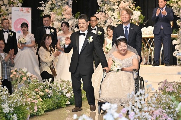 김이강 광주 서구청장이 24일 서구 위더스웨딩홀에서 열린 서구 아너스 장애인 웨딩지원 ‘당신의 특별한 날 드림(dream) 웨딩’에서 휠체어를 밀어주며 신랑, 신부와 함께 입장하고 있다. 광주 서구 제공