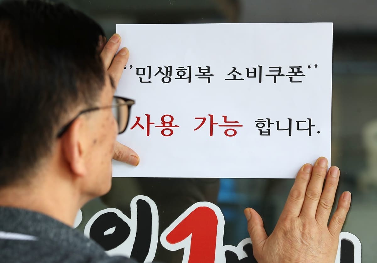 대구 중구의 한 음식점 주인이 출입문에 민생회복 소비쿠폰 사용 가능 안내문을 붙이고 있다. / 뉴스1