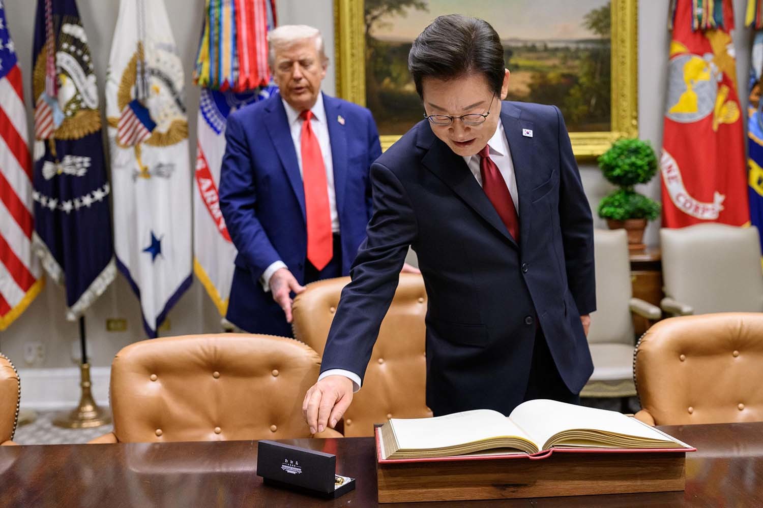 지난 8월 25일(현지시각) 이재명 대통령이 한미정상회담에 앞서 미 백악관 루즈벨트룸에서 방명록에 서명하려고 펜을 잡으려는 순간 도널드 트럼프 미국 대통령이 뒤에서 의자를 당겨 주고 있다. / 백악관 제공.
