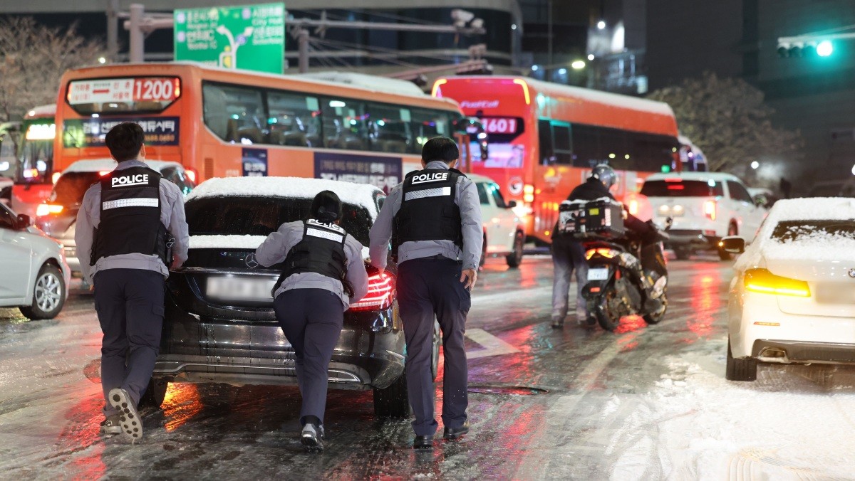 지난 4일 제설작업이 완료되지 못한 도로에서 경찰들이 언덕길 차를 밀고 있다./ 연합뉴스