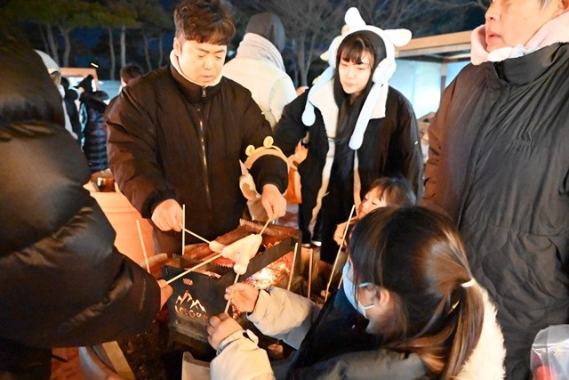 관광객들이 긴 꼬챙이에 꽂은 마시멜로를 노릇노릇하게 구워먹고 있다.