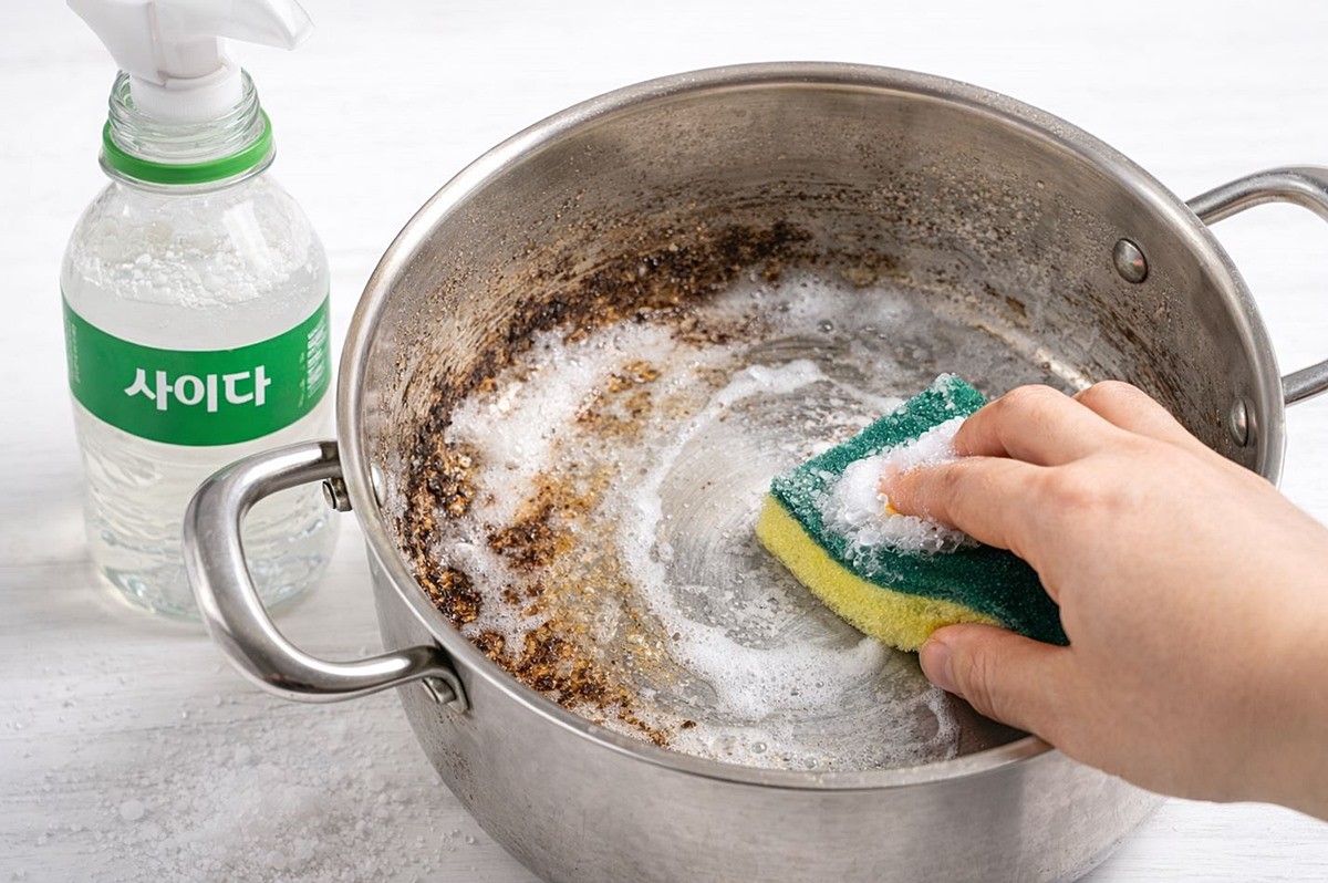사이다와 소금을 섞은 용액을 스펀지에 묻혀 냄비의 찌든 때를 제거하는 모습. 기사 이해를 돕기 위해 AI를 활용해 제작한 자료 사진입니다. 실제 모습과 다소 차이가 있을 수 있습니다.