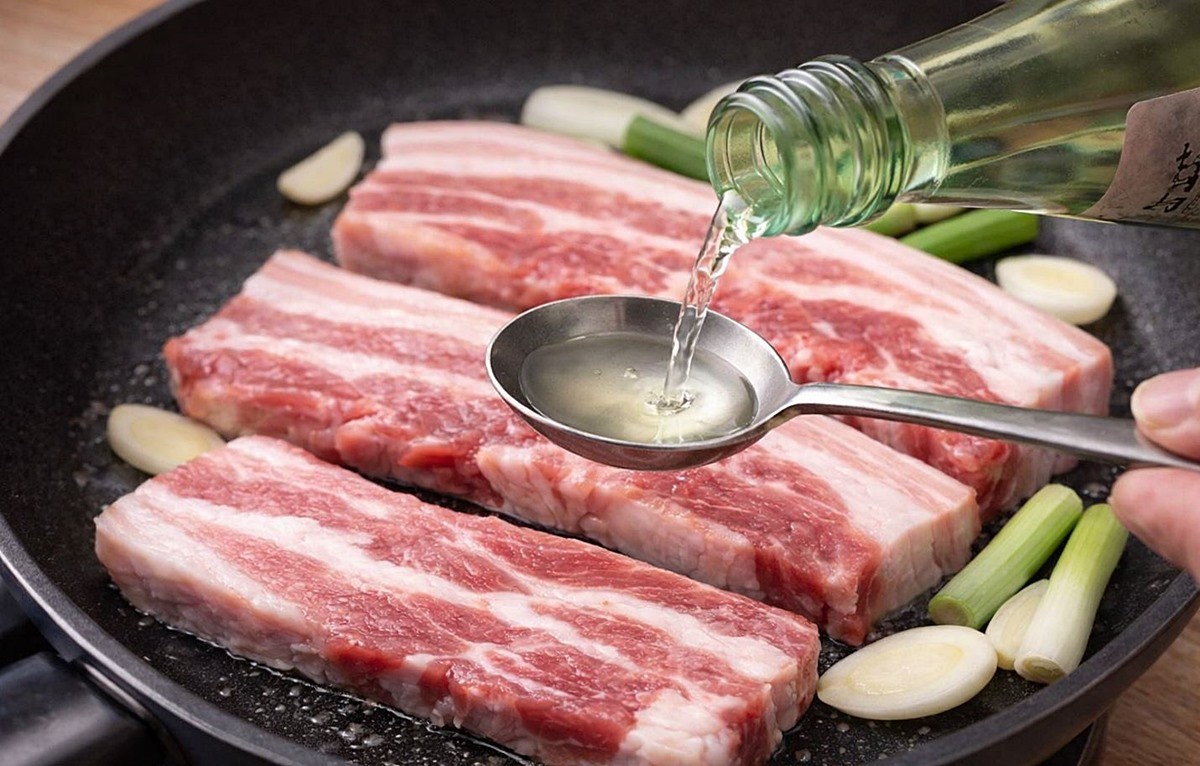 삼겹살에 소주 대신 청주를 넣는 모습. 소주가 알코올 자체의 힘으로 잡내를 눌러 주는 데 초점이 맞춰져 있다면 청주는 발효에서 오는 부드러운 향과 감칠맛이 함께 더해져 고기의 맛을 깔끔하게 살리는 방향으로 작용한다. 기사 이해를 돕기 위해 AI를 활용해 제작한 자료 사진. 실제 모습과 다소 차이가 있을 수 있다.