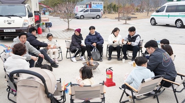 가족 단위 관광객들이 캠핑형 쉼터에 모닥불을 중심으로 모여 앉아 축제를 즐기고 있다