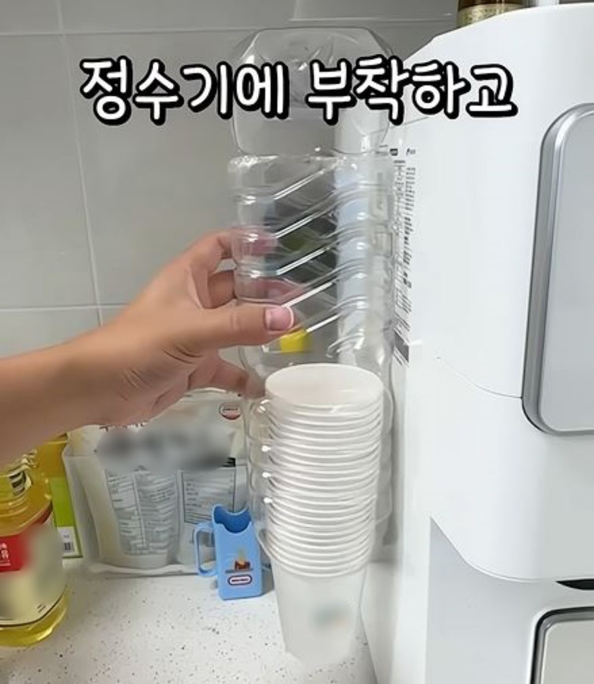 완성된 '페트병 디스펜서'를 정수기 옆에 붙이는 모습. / 유튜브 '살림모드'