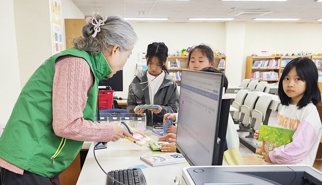 선배교직원 자원봉사자가 학교도서관에서 학생들에게 도서를 대출 해주고 있다