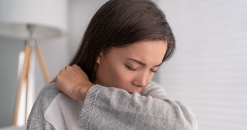 밝고 깨끗한 실내에서 한 젊은 여성이 기침이나 재채기를 참으려는 듯 자신의 옷소매 안쪽으로 입을 가리고 있다 / 셔터스톡