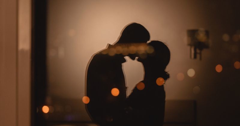 따뜻한 조명이 비치는 아늑한 분위기 속에서 한 커플이 서로를 마주 보며 로맨틱한 입맞춤을 나누는 실루엣이 담겨 있다 / 셔터스톡