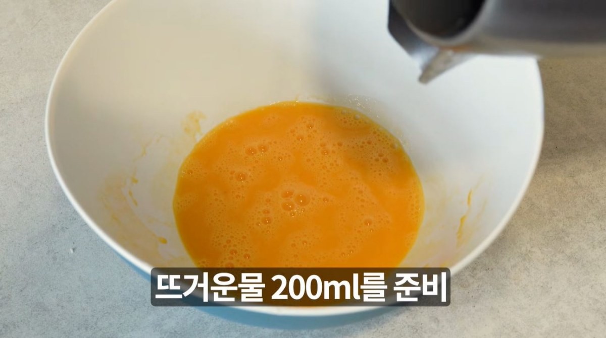 계란물에 뜨거운 물 200ml를 넣으려는 모습. 뜨거운 물을 넣으면 계란이 익는 시간이 단축되고, 식감이 촉촉하고 몽글몽글해져 더 맛있어 진다. / 유튜브 '리꼬 Rico'
