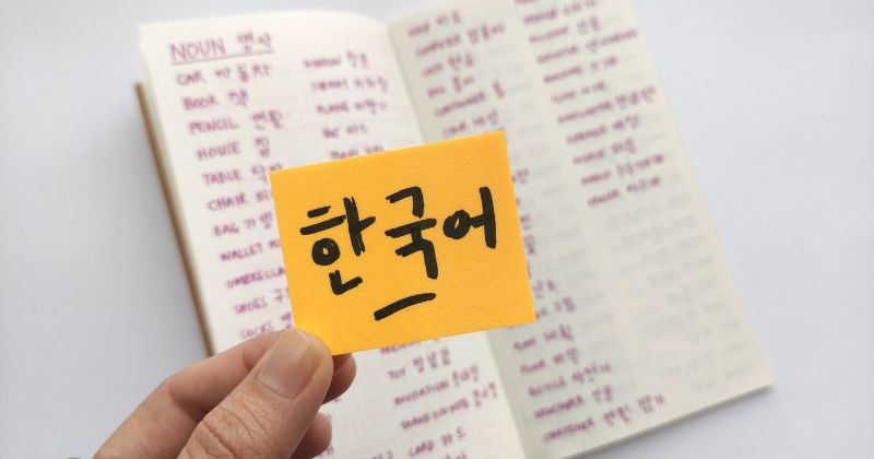 끈적끈적한 노트 위의 한국어는 한국어를 뜻하는데 한국동사가 가득한 수첩을 배경으로 하고 있다 / 셔터스톡