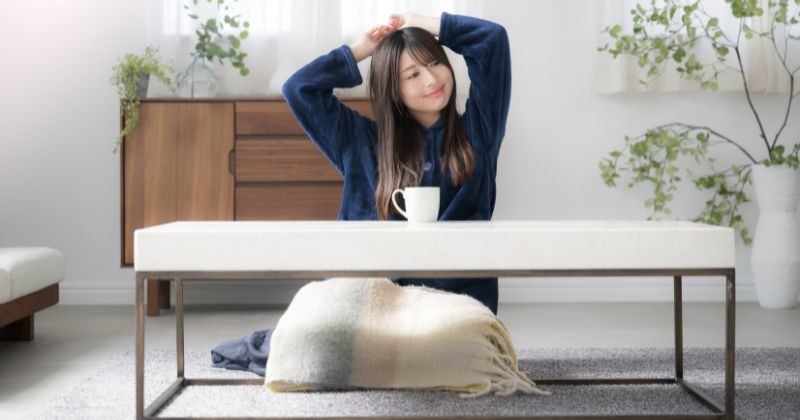 그녀의 거실에 앉아 스트레칭을 잠옷 입은 젊은 일본 여성. 늦게 일어났어 가을이나 겨울 아침에 휴식을 취하세요. 광각 전면 뷰 / 셔터스톡