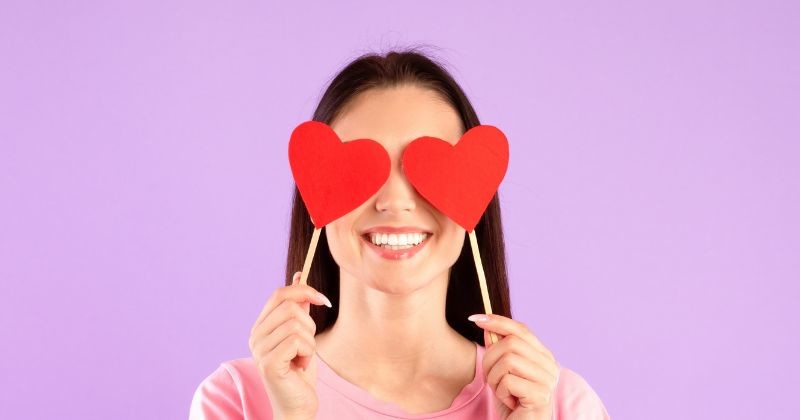 사랑에 눈이 멀었지 보라색 스튜디오 배경 위에 포즈 두 빨간 종이 하트를 손에 들고 긍정적인 젊은 여자의 초상화, 그녀의 눈을 덮고 미소 행복 한 애정 숙녀 / 셔터스톡