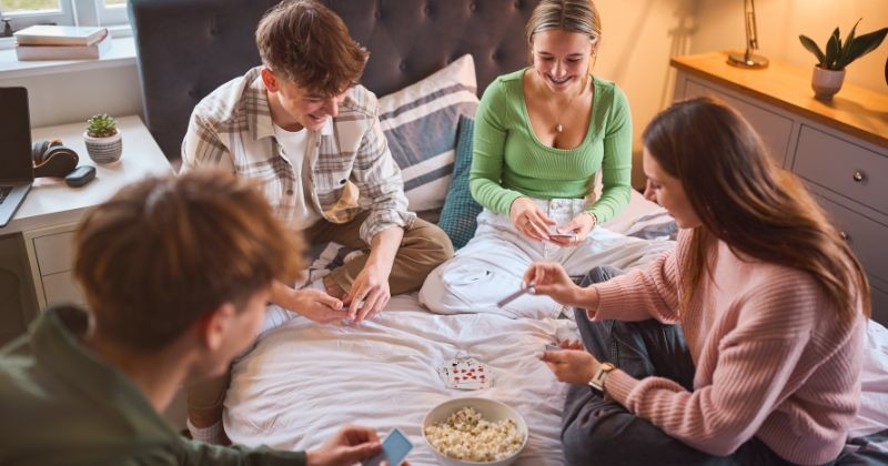 집에서 함께 침실에서 웃고 카드 놀이를 하는 십대 소녀와 소년 그룹 / 셔터스톡