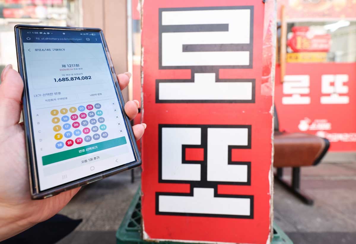 모바일 로또 판매가 시작된 지난 2월 서울 시내의 한 복권 판매점 앞에서 시민이 휴대폰으로 로또를 구매하고 있다. 이용자는 모바일 동행복권 홈페이지에 가입한 뒤 예치금을 충전하면 오전 6시부터 자정까지 복권을 살 수 있다. 시범 운영 기간인 이번 상반기에는 평일에만 회차당 1인 5000원까지 구매할 수 있으며 PC 온라인 구매 금액과 합산해 계산된다. 전체 온라인 판매 규모도 전년도 로또 판매액의 5% 이내로 묶여, 한도에 도달하면 판매가 자동 중단된다. / 뉴스1