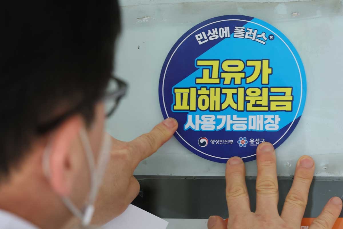 고유가 피해지원금 신청을 앞두고 23일 대전 유성구 한 식당 주인이 피해지원금 사용가능매장 안내문을 붙이고 있다. 이번 지원금은 소득 하위 70%를 대상으로 1인당 15만 원에서 최대 60만 원까지 차등 지급된다. 1차 신청은 오는 27일부터 기초생활수급자·차상위계층·한부모 가구를 대상으로 진행되며, 2차 신청은 5월 18일부터 7월 3일까지 이어진다. 지원금은 신용·체크카드 또는 대전사랑카드 중 선택해 받을 수 있으며, 주소지 관할 동 행정복지센터나 제휴 은행 영업점을 방문해 신청할 수 있다. 유성구는 24일부터 피해지원금 전용 콜센터와 13개 동 행정복지센터를 통해 신청 안내와 현장 지원을 실시한다. / 뉴스1