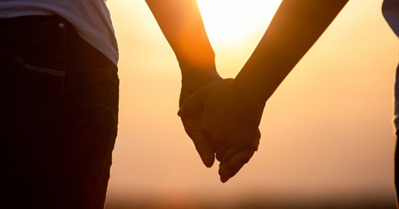 노을을 배경으로 손을 잡고 있는 젊은 사랑 커플 실루엣을 클로즈업한다. / 셔터스톡