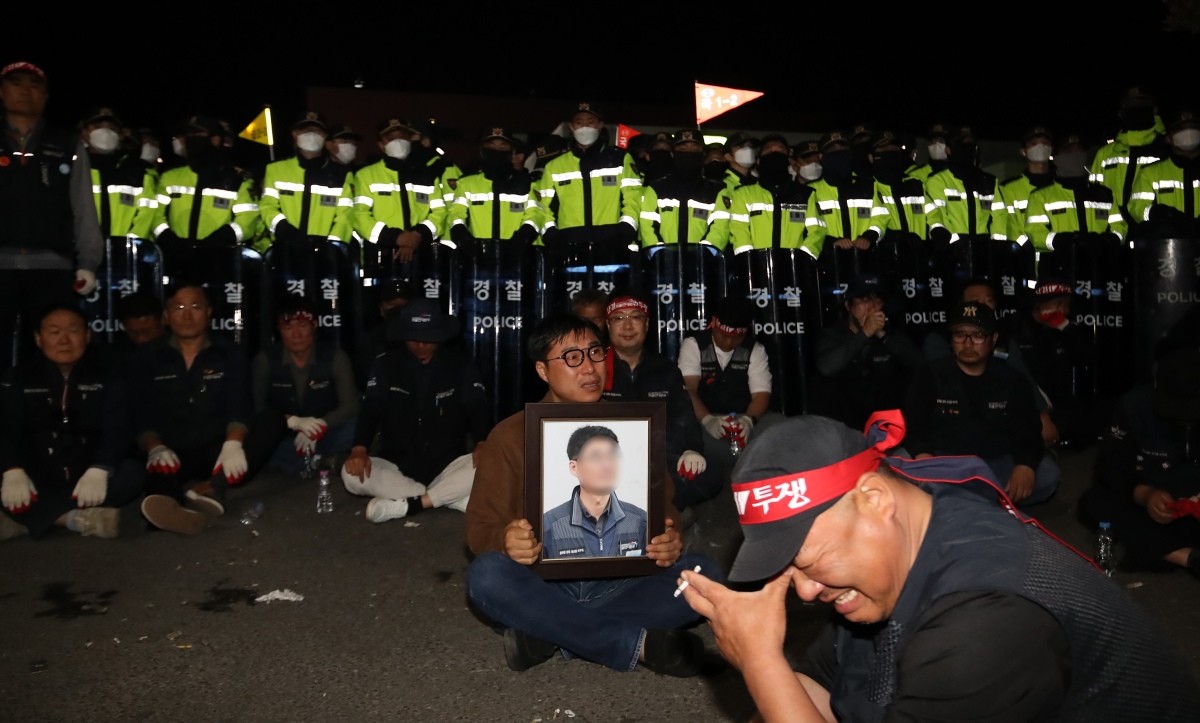 지난달 20일 경남 진주시 정촌면 CU 진주물류센터 앞에서 화물연대 노조원이 집회 중 2.5톤 화물차에 치어 숨진 노조원의 영정을 들고 슬픔에 잠겨 있다.