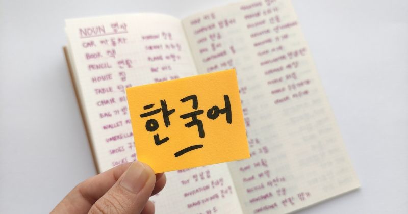 끈적끈적한 노트 위의 한국어는 한국어를 뜻하는데 한국동사가 가득한 수첩을 배경으로 하고 있다. 한국어 초보자를 위한 기본 단어 / 셔터스톡