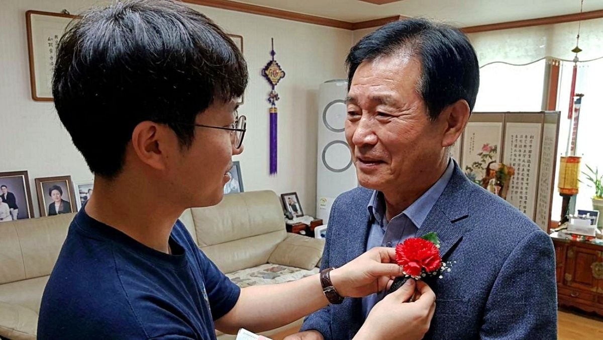 아버지 가슴에 카네이션을 달아드리며 현금이 담긴 봉투를 함께 건네고 있는 모습. 기사 내용 토대로 AI툴 활용해 제작한 자료사진.