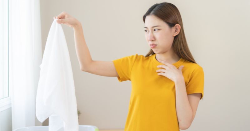 한 여성이 옷 냄새를 맡고 불쾌한 표정을 짓고 있다. / 셔터스톡