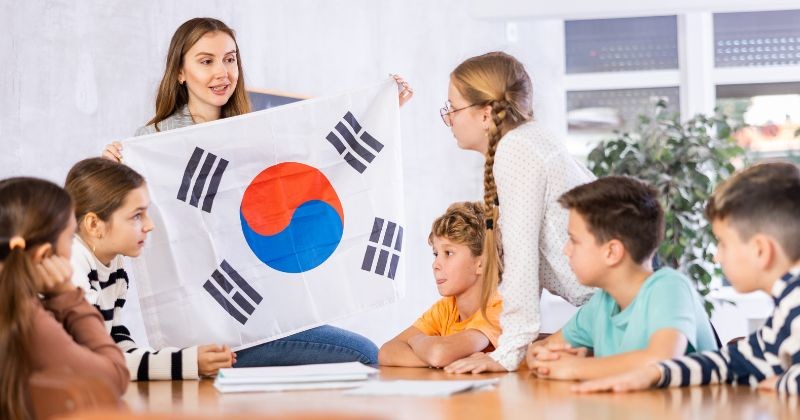 학생들은 한국에 대한 이야기를 주의 깊게 듣습니다. 선생님은 손에 태극기를 들고 계신다 / 셔터스톡