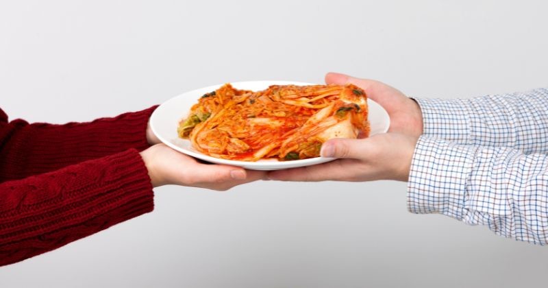 두 사람이 김치가 담긴 접시를 함께 건네고 있는 장면. / 셔터스톡