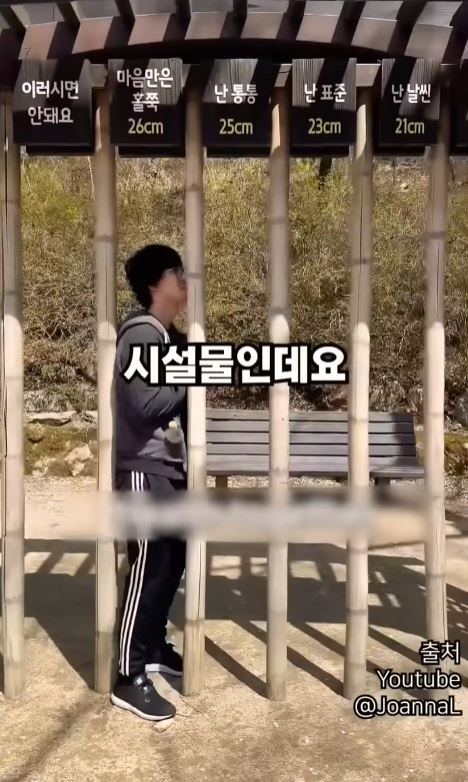 남성은 대나무 모양의 기둥들 사이에 몸을 끼워 넣은 채 옆을 바라보고 있으며, 통과하기 위해 애쓰는 듯한 자세를 취하고 있습니다 / JoannaL 유튜브