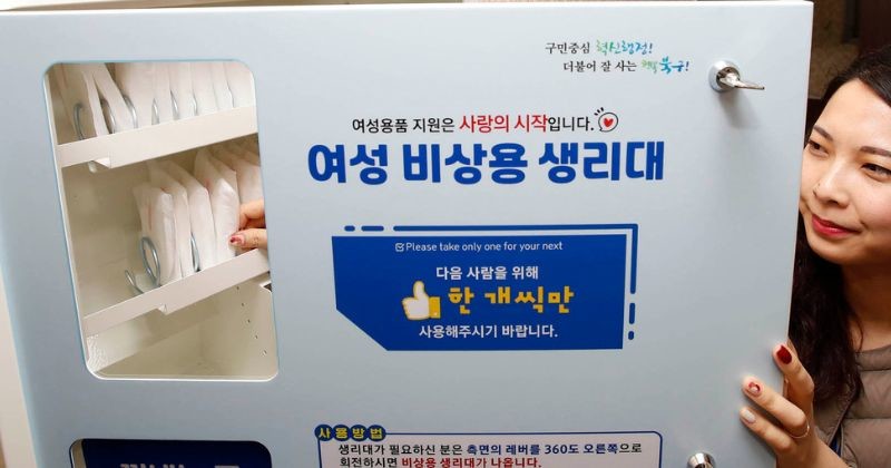 여자화장실에서 여성아동과 직원이 위생용품 무료지급기에 위생용품을 비치하고 있다 / 뉴스 1