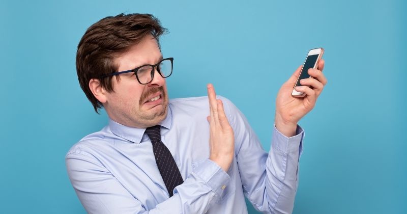 심각한 통화를 피하려고 셔츠와 핸드폰을 들고 있는 젊은 남자.그는 전화상으로 해고되는 것을 두려워한다. / 셔터스톡