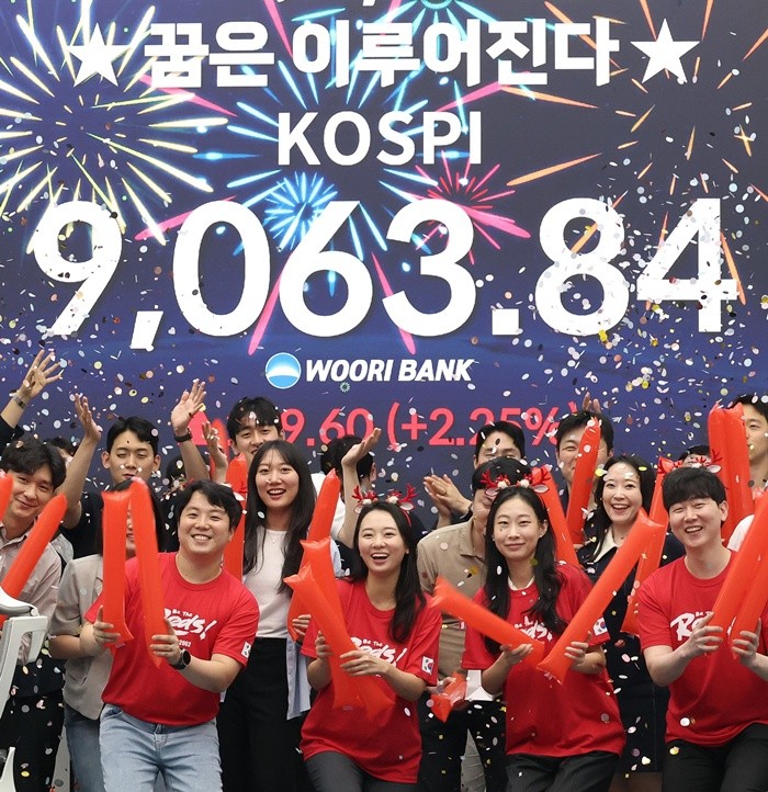 코스피 지수가 전인미답의 9000선 고지를 돌파한 18일 오후 서울 중구 우리은행 본점 딜링룸에서 직원들이 코스피 종가를 배경으로 축하 세리머니를 하고 있다. 코스피는 이날 전일 대비 199.60포인트(2.25%) 오른 9063.84에 장을 마쳤다. 한국 증시는 반도체 대형주의 폭발적인 상승세에 힘입어 지난 5월 26일 장중 8000선을 돌파한 후 불과 16거래일 만에 천의 자리를 바꾸며 '9천피' 시대에 진입했다. 2026.6.18/뉴스1