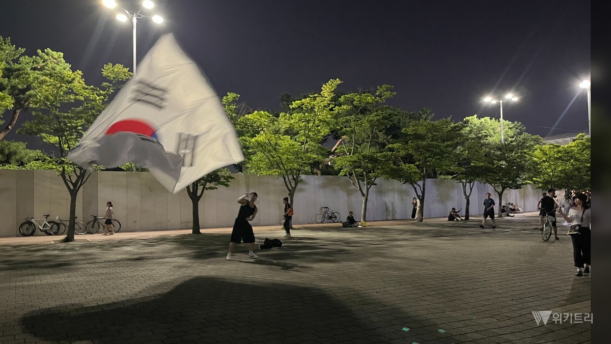 올림픽공원 집회 현장에서 한 청년 참가자가 대형 태극기를 흔들고 있다. / 위키트리