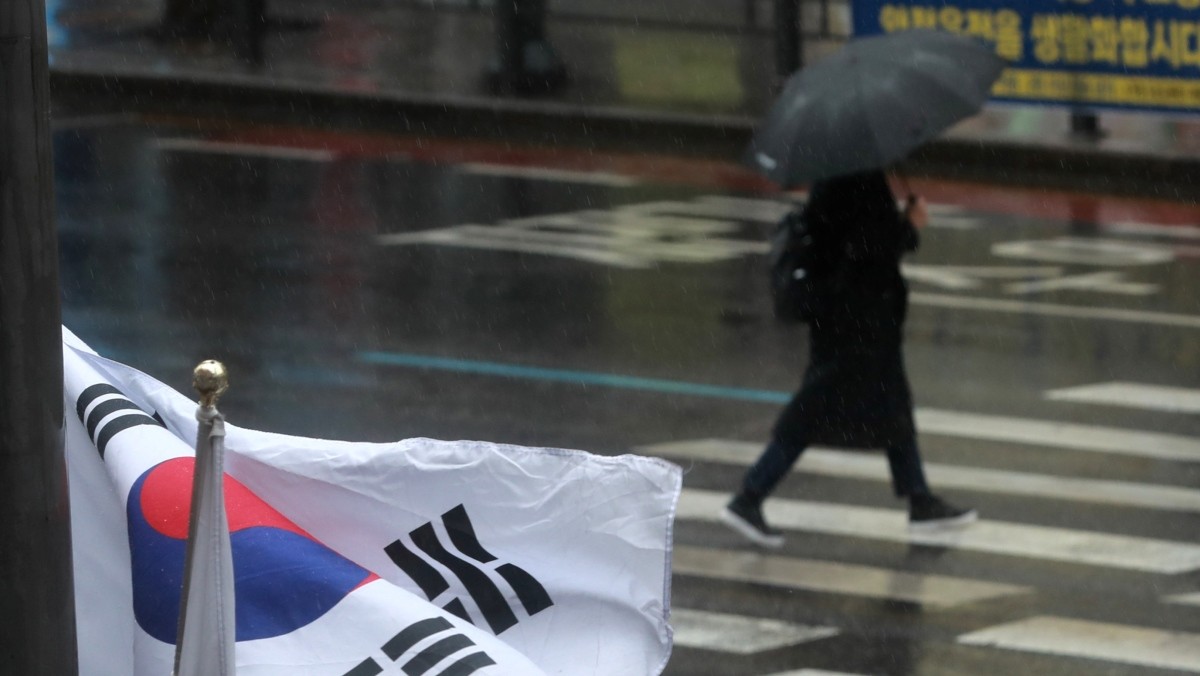 태극기 뒤로 한 시민이 우산을 쓰고 걷고 있다. / 뉴스1