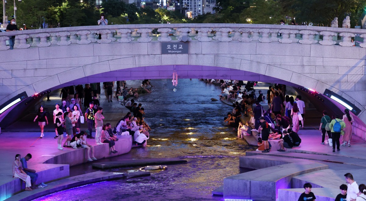 서울 전역에 폭염주의보와 열대야주의보가 동시 발효된 지난 26일 저녁 서울 중구 청계천을 찾은 관광객과 시민들이 물가에 앉아 더위를 식히고 있다. / 뉴스1