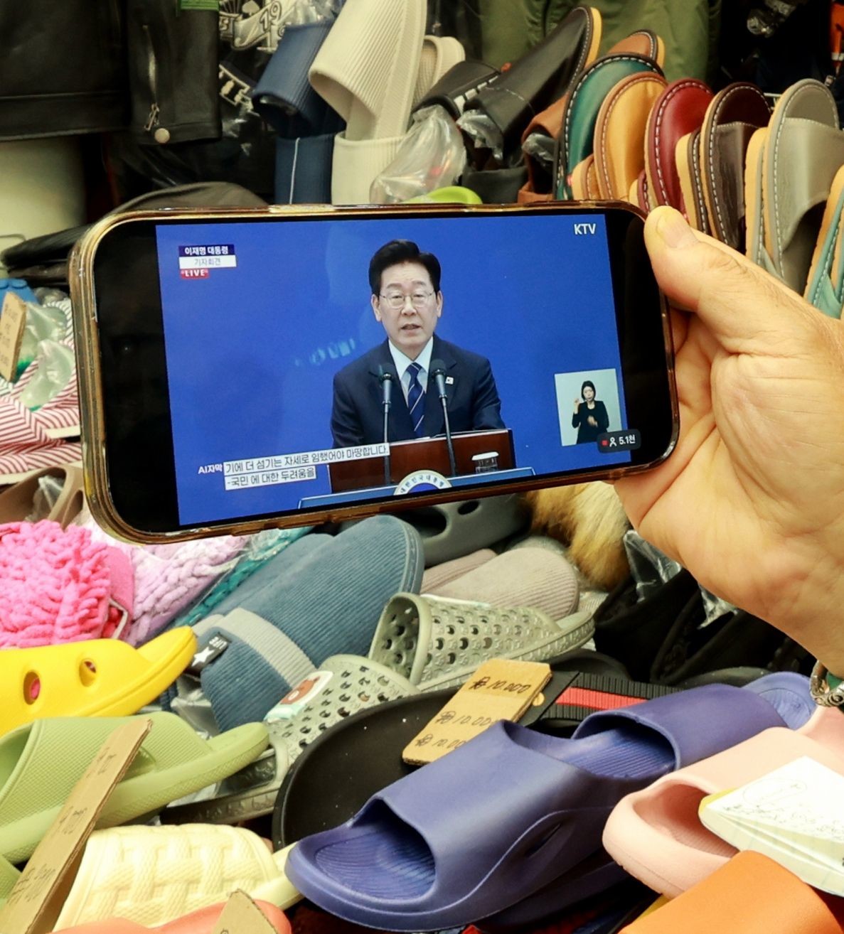 지난 18일 서울 한 전통시장에서 상인이 핸드폰으로 이재명 대통령의 기자회견 뉴스를 지켜보고 있다. / 뉴스1
