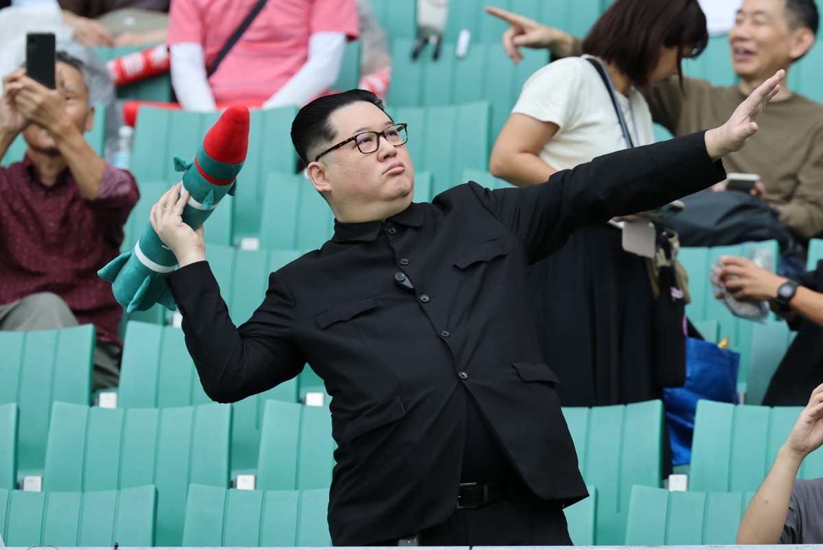 21일 일본 시즈오카 스타디움 에코파에서 열린 2026 아이치·나고야 아시안게임 조별예선 F조 대한민국과 북한의 경기를 찾은 중국계 정치활동가 '하워드X'가 북한 김정은 국무위원장이 로켓을 든 모습을 표현하고 있다. / 뉴스1