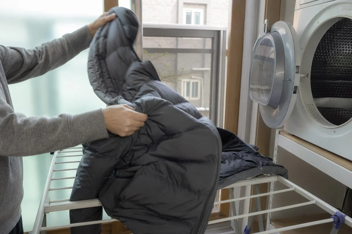건조기 앞에서 검은색 패딩을 건조대 위에 올리는 모습 — AI 자료 이미지