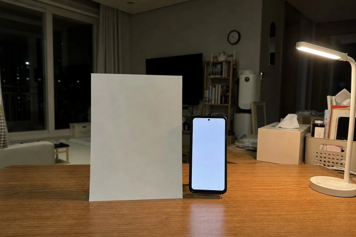 나무 책상 위 흰 종이와 밝은 화면의 스마트폰을 나란히 세워 둔 모습 — 이해를 돕는 AI 자료 이미지