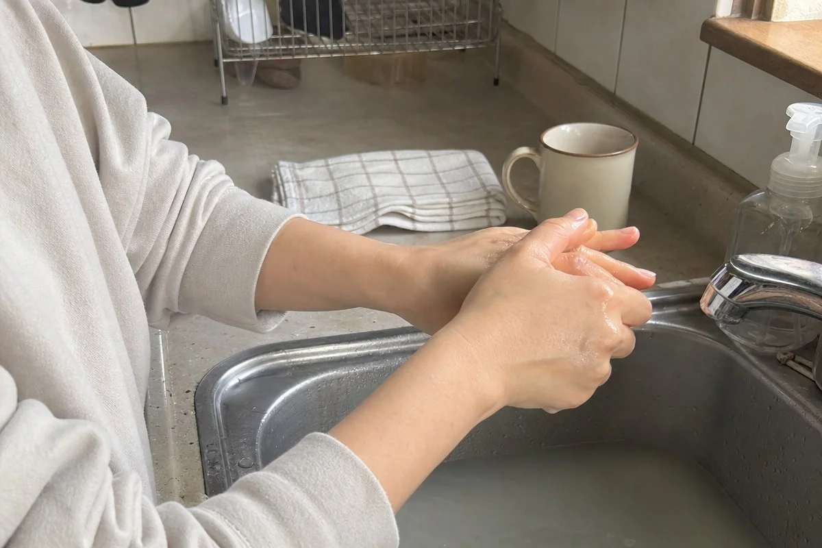 주방 싱크대 앞에서 양손가락을 맞대고 따뜻한 물에 씻는 모습 — AI 자료 이미지