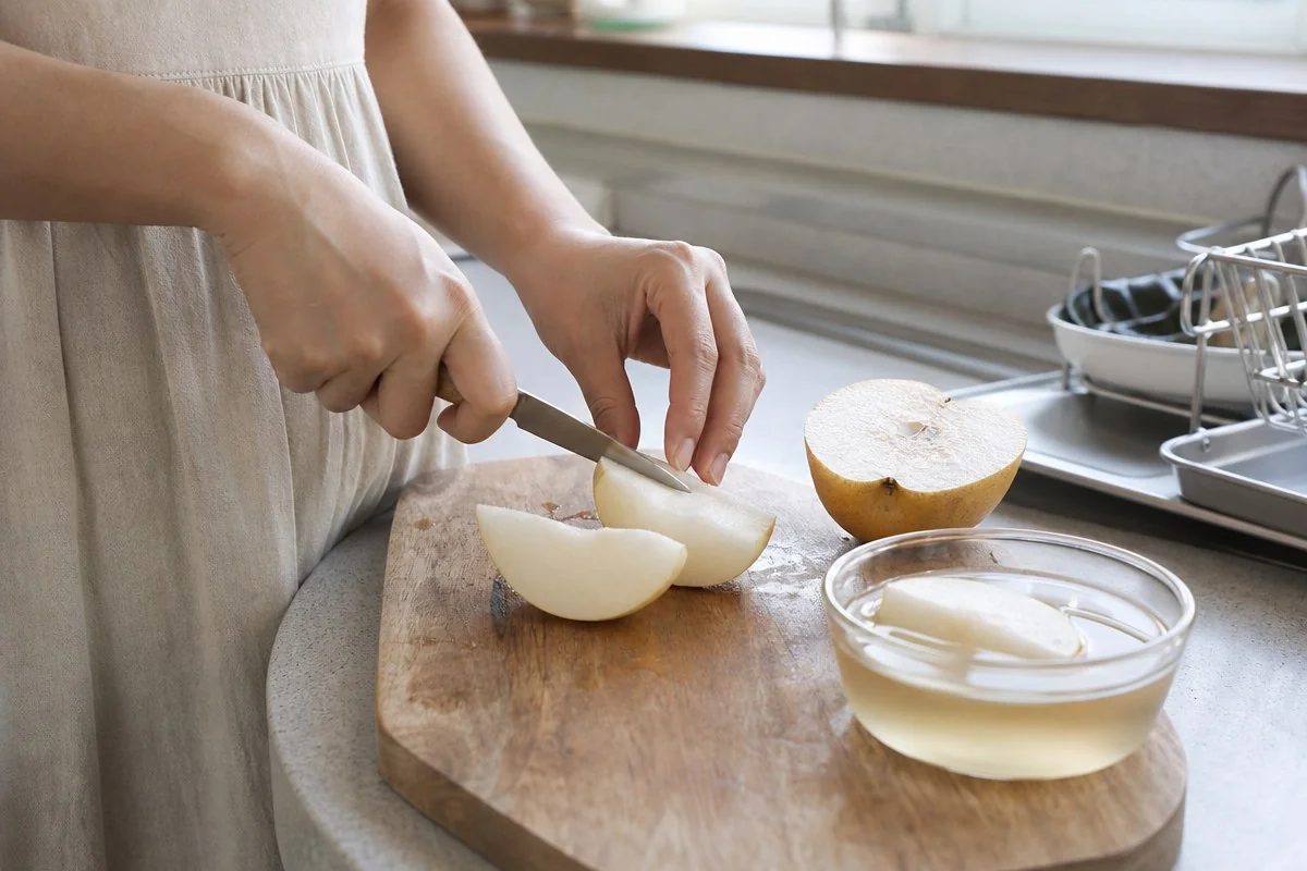 주방 도마 위 배를 칼로 자르고 옆에 물그릇을 둔 모습 — AI 자료 이미지