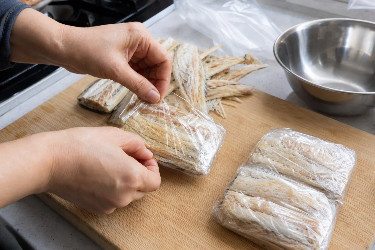 주방 조리대에서 비닐랩으로 과메기를 감싸 포장하는 모습 — 이해를 돕는 AI 자료 이미지